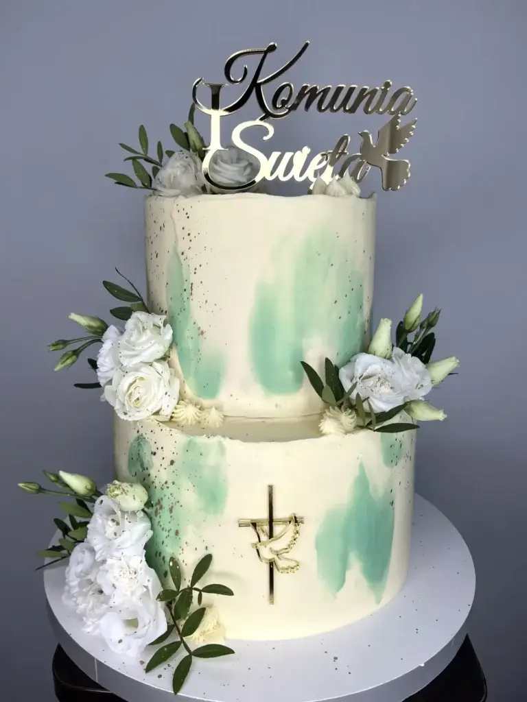 Elegancki dwupiętrowy torty na Chrzest Święty ozdobiony białymi różami, złotym krzyżem oraz toperem na górze.