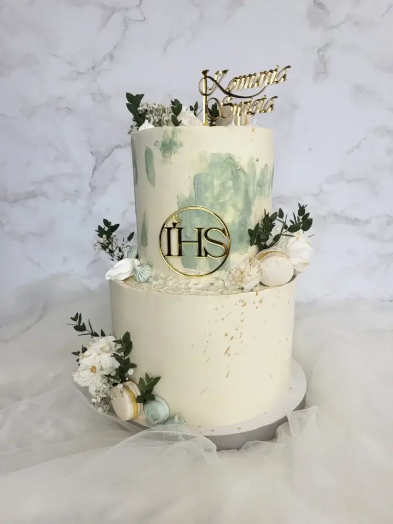 Dwupiętrowy tort z białymi różami oraz białymi makaronikami, ozdobiony dwoma toperami w kolorze złotym oraz liśćmi eukaliptusa