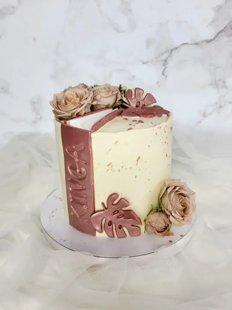 Elegancki tort w kształcie książki z dekoracją metalicznych liści i róż w odcieniach pudrowego różu