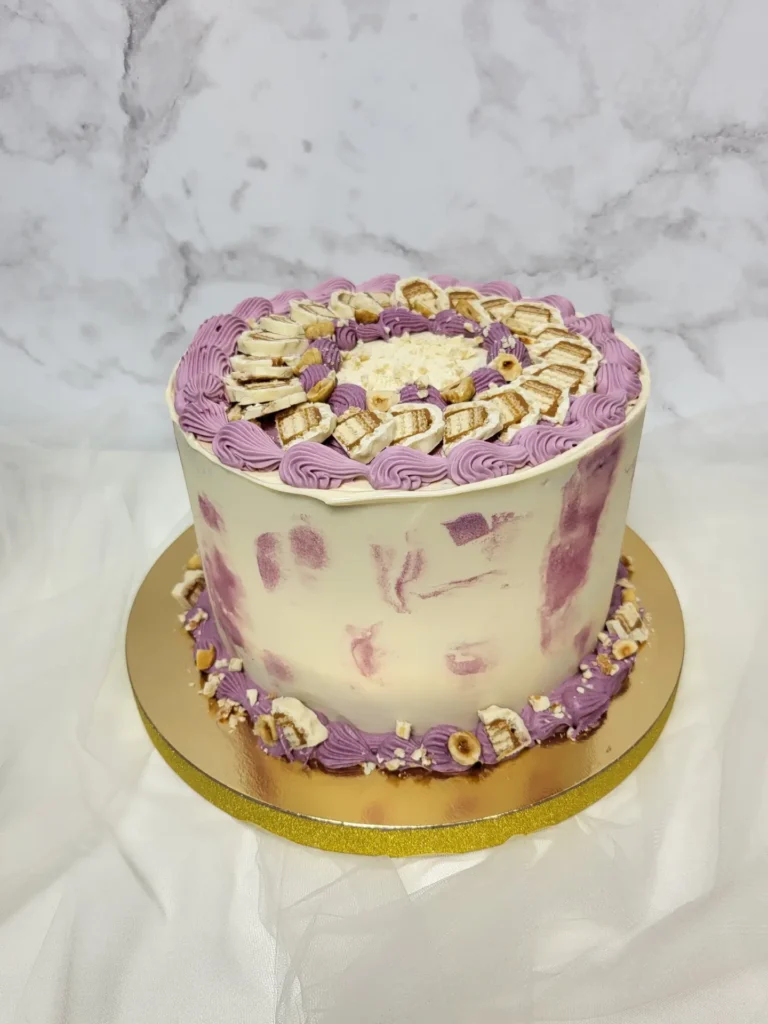 Klasyczny tort z fioletowymi rozetkami oraz białym pokrojonym batonem lion